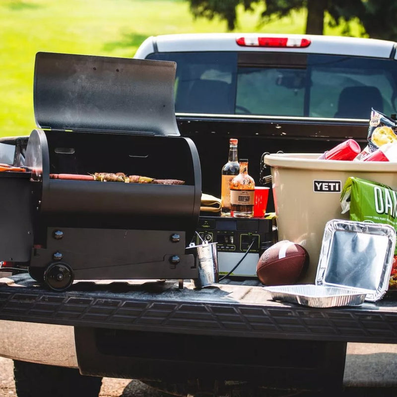 Traeger Tailgater in a truck bed with a Yeti bucket and assorted picnic goods